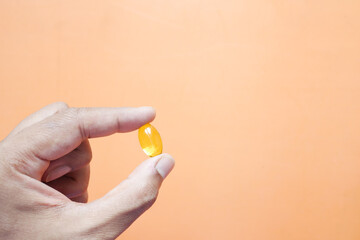 holding fish oil supplement on orange background 