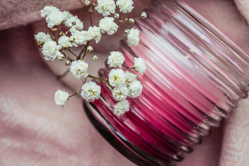 A branch of white little flowers is near a off candle, placed on a cozy pink scarf. Warm atmosphere.
