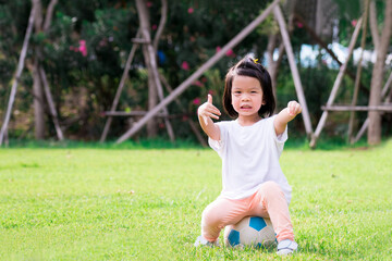 Portrait image of 4 baby kid. Happy Asian child girl sitting on white-blue football. Children gave a thumbs up showing that it was great. Learning sport and playing concept. Smiling little toddler.