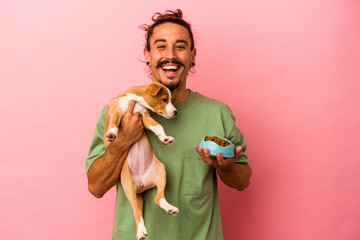 Young caucasian man holding his puppy and his food isolated on pink background