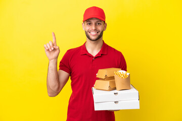 pizza delivery man picking up pizza boxes and burgers over isolated background pointing up a great...