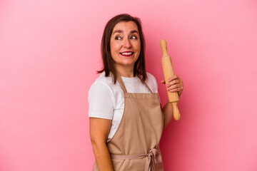 Middle age pastry chef woman isolated on pink background looks aside smiling, cheerful and pleasant.