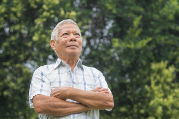 Naklejka na ściany i meble Senior man arms crossed, smiling, and looking up while standing in a garden. Elderly Asian man happiness after retirement. Space for text. Aged people and relaxation concept