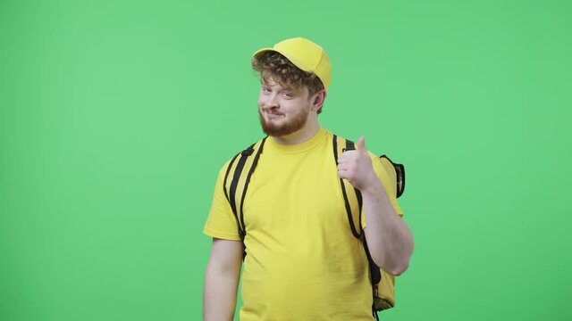 Portrait of young men pointing side hand for something then nods and shows thumb like. Redhead male in yellow delivery courier uniform posing on green screen. Close up. Slow motion ready 59.97fps.