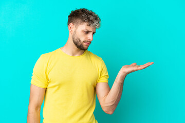 Young handsome caucasian man isolated on blue background holding copyspace with doubts