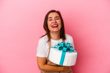 Middle aged pastry chef woman holding a cake isolated on blue background laughing and having fun.