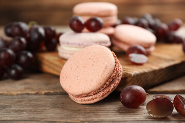 Delicious macarons and grapes on wooden table, closeup