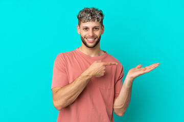 Young handsome caucasian man isolated on blue background holding copyspace imaginary on the palm to...