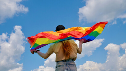 Bisexual, lesbian, woman, transgender holds LGBT flag against blue sky with clouds on a sunny day...