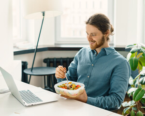 Satisfied male employee eating vegetarian food, pasta with vegetables, holding plastic container...