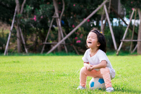 Portrait image of 4 baby child. Happy Asian kid girl sitting on white-blue ball on nature green park. Children laughing and close her eyes. Learning sport and exercise concept. Smiling little toddler.