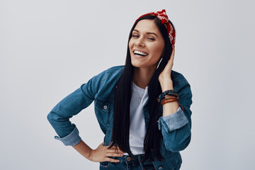 Funky young woman in bandana looking at camera and smiling while standing against grey background