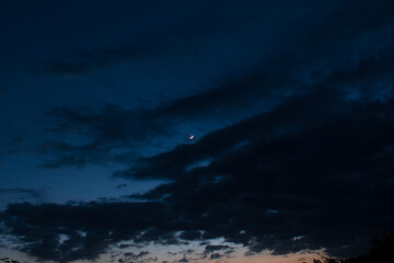 Fototapeta na wymiar Silhouette picture of dark cloudy blue sky and waxing crescent moon in middle