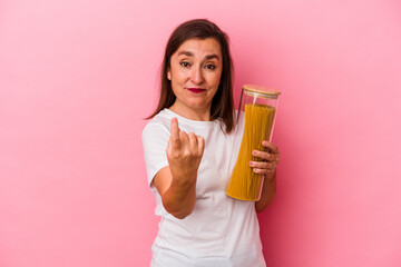 Middle age caucasian woman holding a pasta jar isolated on pink background pointing with finger at you as if inviting come closer.