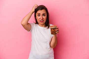 Middle age caucasian woman holding an almond jar isolated on pink background being shocked, she has remembered important meeting.