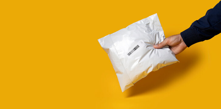 Delivery guy holding white polythene envelope against yellow background