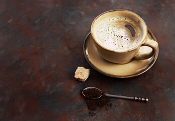 Cup of coffee and ground coffee beans in a spoon on a dark background with space for free text.