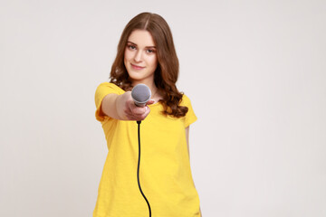 Young attractive female with brown wavy hair wearing yellow casual T-shirt posing with microphone...
