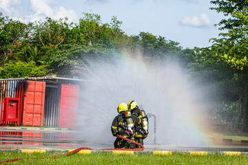 Fototapeta premium Two firefighter water spray by high pressure nozzle in fire fighting operation. Fire and rescue training school regularly to get ready.