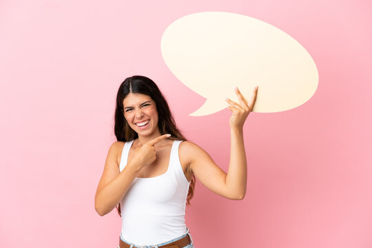 Young caucasian woman isolated on pink background holding an empty speech bubble and pointing it