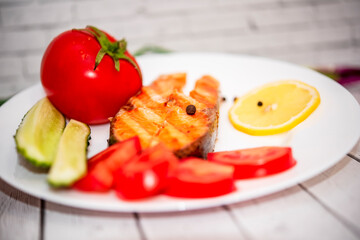 fried piece of salmon on a white plate with tomatoes, onions, cucumbers, on the boards