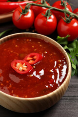 Spicy chili sauce in bowl on wooden table, closeup