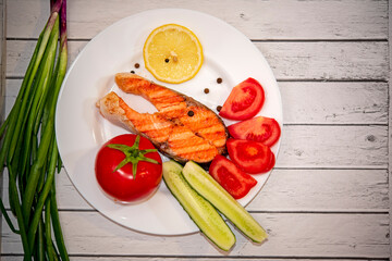 fried piece of salmon on a white plate with tomatoes, onions, cucumbers, on the boards