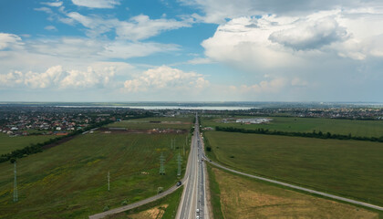 From the height of the flight, a spacious view of the highway between green fields and villages on a summer day in cloudy weather