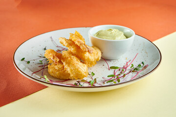 Appetizer - tempura fried shrimps with sauce in a white plate on colored backgrounds. Fingerfood, pub