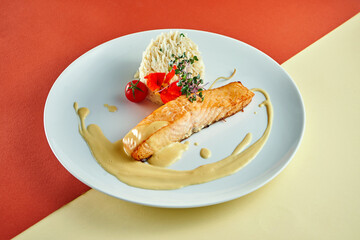 Stir-fried salmon steak with yellow sauce and rice on a side dish in a white plate on colored backgrounds.