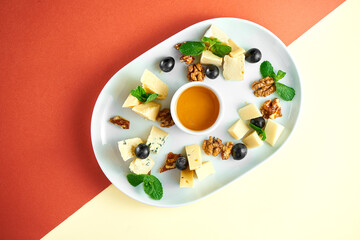 Appetizer - antipasti cheese plate with dorblu, parmesan and camembert, honey, nuts on bright colored backgrounds