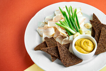 Ukrainian appetizer sliced bacon (salo) with rye bread and mustard on a white plate on bright colored backgrounds