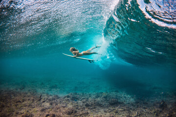 beautiful woman in the bikini doing duck dive with the surfboard under the breaking waves in the clear water of the Indian Ocean  - obrazy, fototapety, plakaty