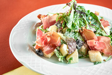 Delicious mix salad with jamon and pear in a white plate on bright colored backgrounds