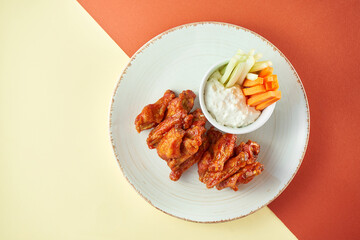 Wings in barbecue sauce with white sauce and carrots, cucumber in a white plate on colored backgrounds. Fingerаood and Pub