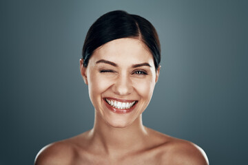 Beautiful young woman looking at camera and smiling while standing against grey background