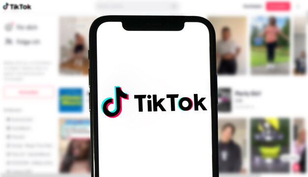 TikTok Logo wird auf einem modernen Smartphone angezeigt, im Hintergrund die Website mit Videos des soziales Netzwerks, Musikvideo, Influencer