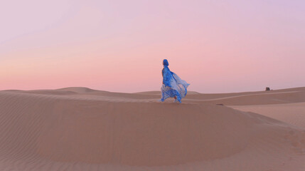 Fototapeta na wymiar Portrait of beautiful Arab woman weared in blue traditional dress in the desert during sunset.