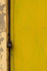 Close-up of yellow painted door and wall with cracked paint, black padlock on closed door