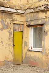 Old residential courtyard with cracked paint, yellow door and window, wires