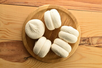 Several white sweet marshmallows on a round bamboo tray on a wooden table, close-up, top view.