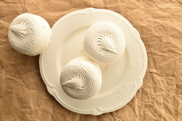 Three sweet marshmallows on a white ceramic plate, on craft paper, close-up, top view.