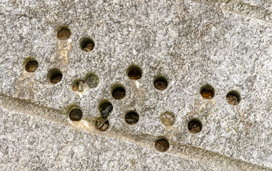 Natural abstract detail of random holes in a granite block located in a breakwater groyne. Tides have partially filled some with natural materials. Landscape image with space for copy. England. - 440768244