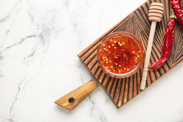 Board with hot honey and dry chili peppers on light background