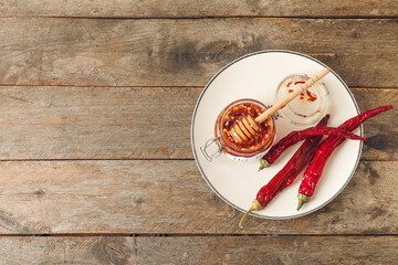Plate with hot honey and chili peppers on wooden background