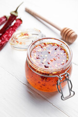 Jar of hot honey and dry chili peppers on light wooden background