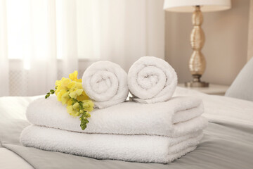 Fresh white towels with flower on bed indoors