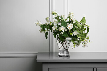 Beautiful bouquet with fresh jasmine flowers in vase on grey table indoors