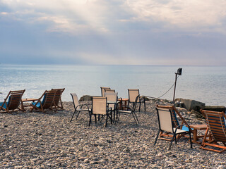 Chairs and tables of a bar on a stone beach with cloudy sky