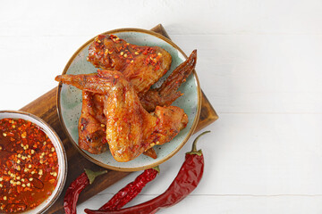 Board with tasty fried chicken wings, dry chili peppers and hot honey on light wooden background